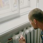 From above side view of crop anonymous male worker with ruler near radiator and windowsill in house